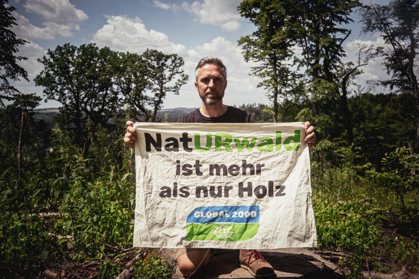 Dominik Linhard mit einem Banner im Wald: "NatURwald ist mehr als nur Holz"