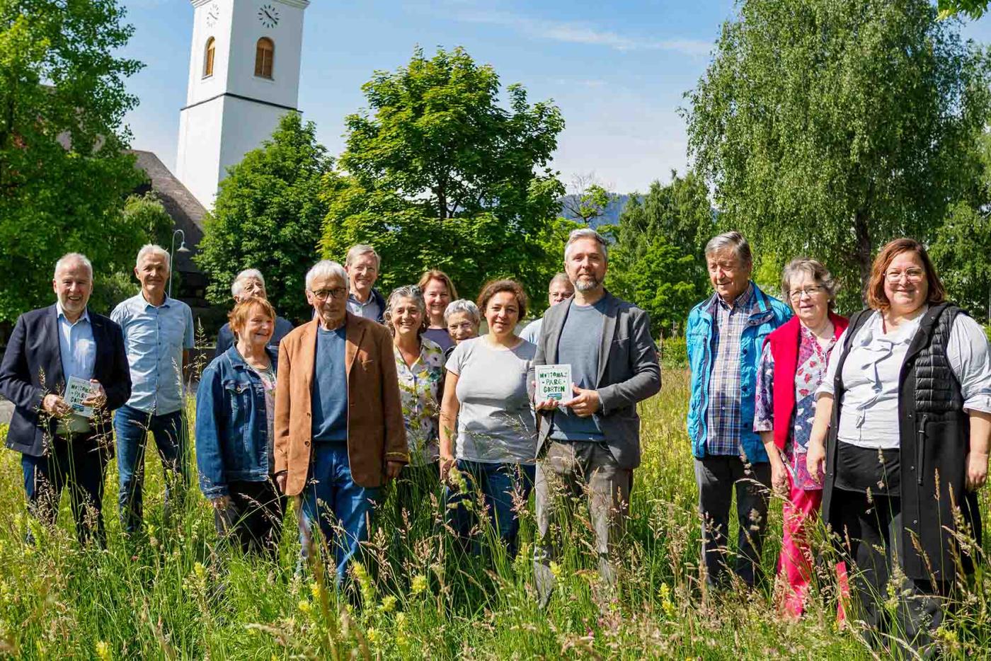 Gemeinde Göfis Mitgleider stehen auf einer Wiese und halten Nationalpark Garten Plakette