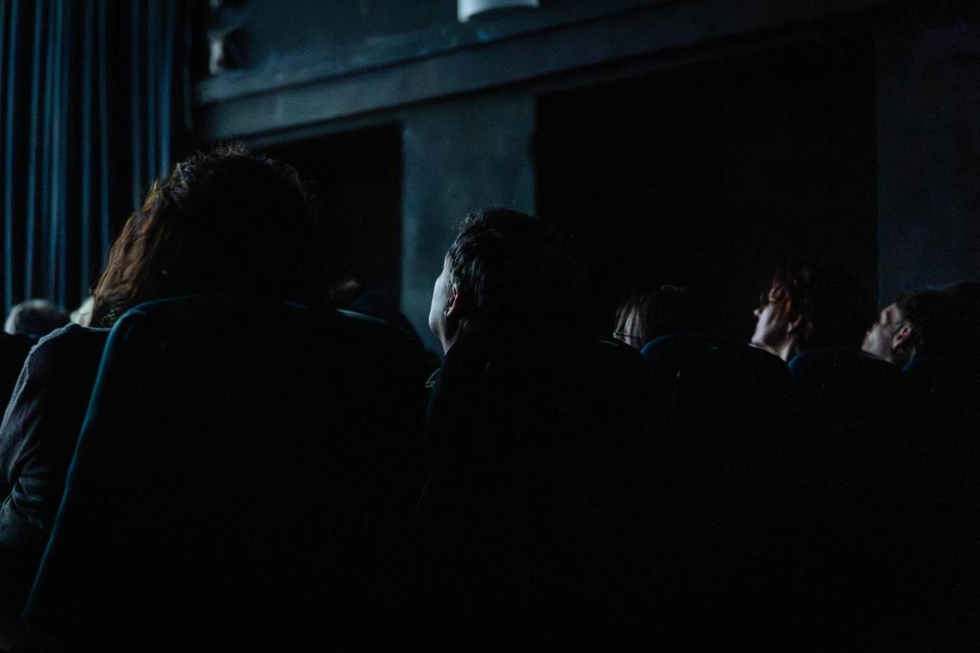 In einem sehr dunklen Kinosaal sieht man schemenhaft Menschen sitzen