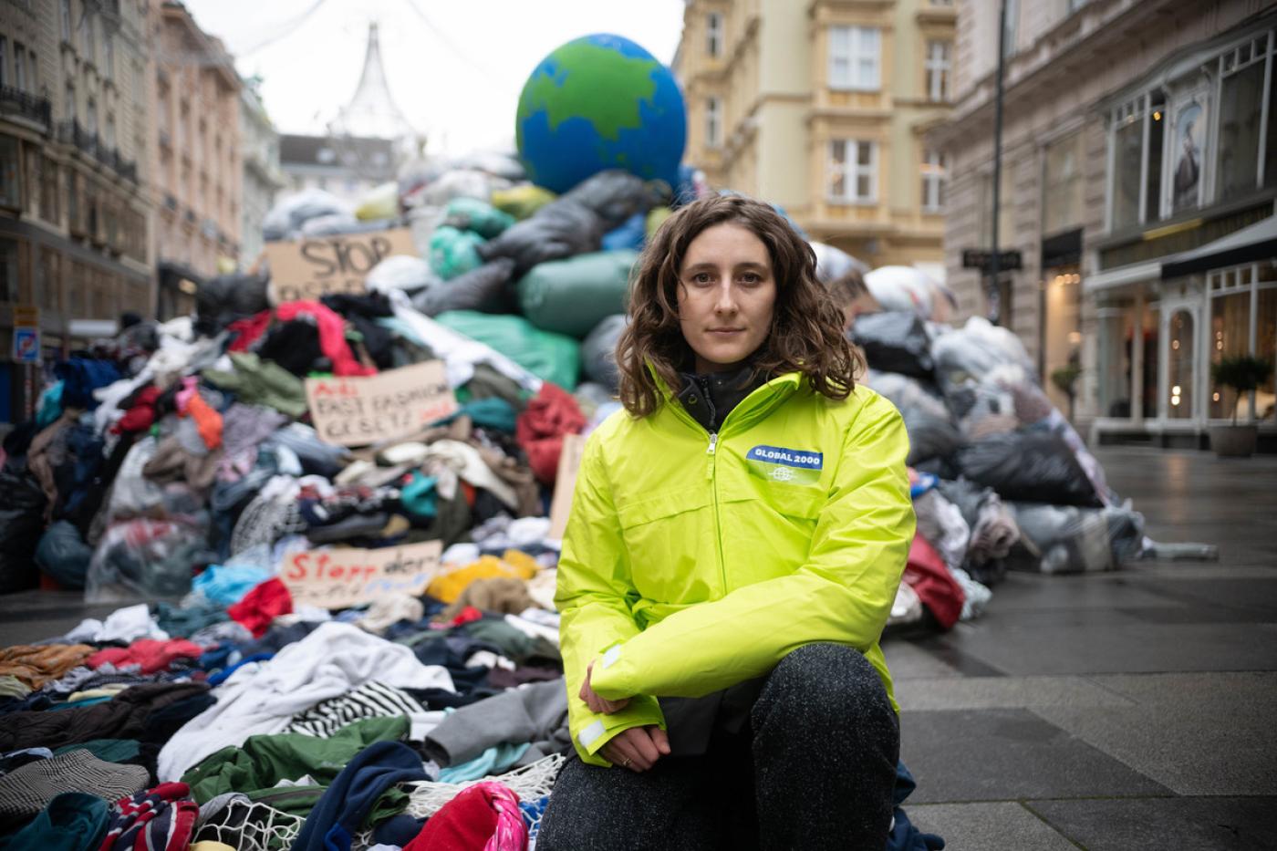 Anna Leitner, Ressourcensprecherin von GLOBAL 2000, hockt vor Müllberg mit Kleidung in der Wiener Innenstadt
