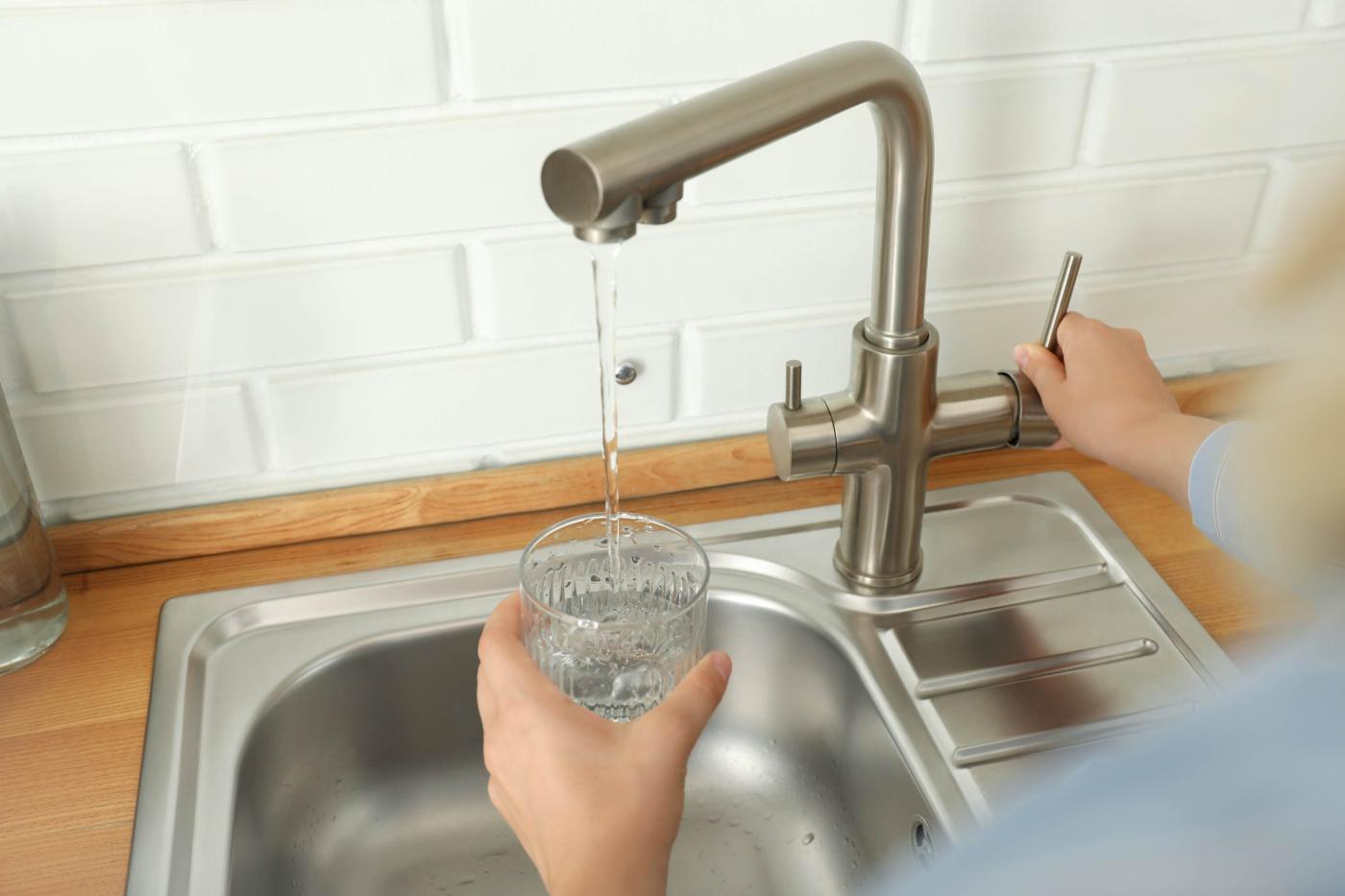 Wasserhahn über Spüle, aus dem Wasser in ein Glas fließt, Hand hält das Glas und betätigt den Hebel