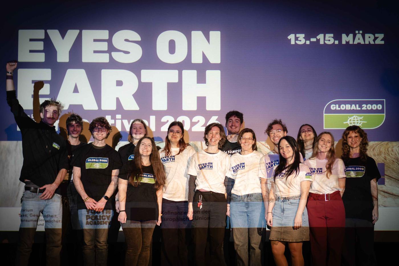 Team*Aktiv steht vor einer Wand mit dem Schriftzug 'EYES ON EARTH Festival 