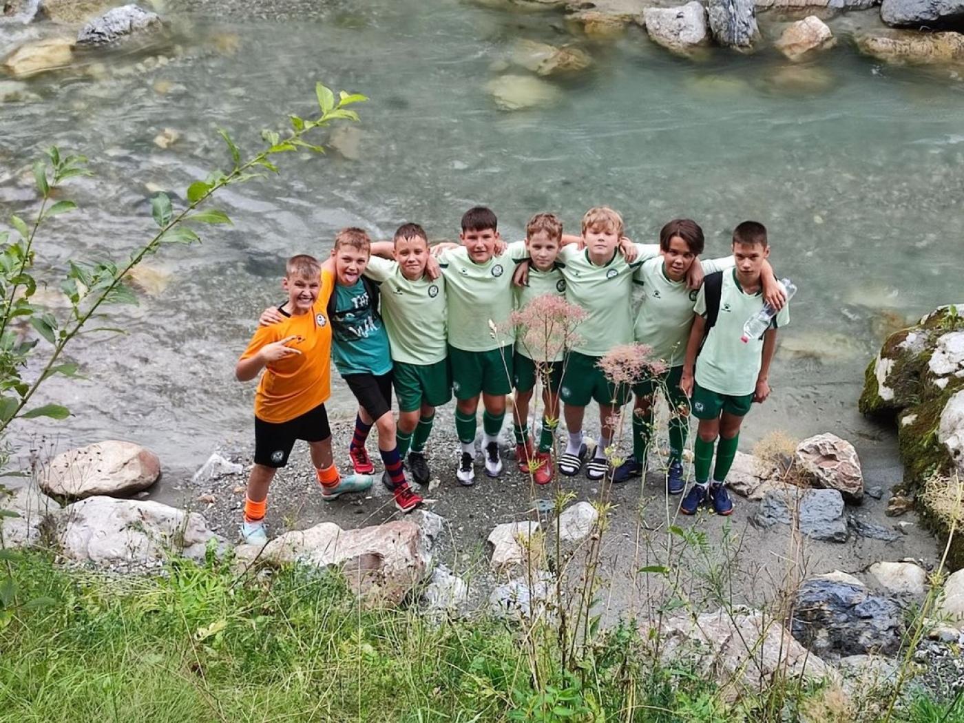 Sieben Jungen in Sportkleidung stehen am Ufer eines Flusses und umarmen sich