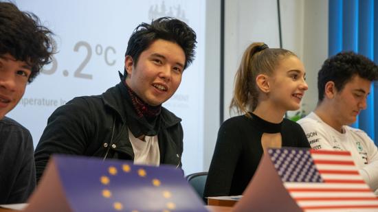 Zwei Schüler:innen sitzen am Pult mit USA und EU Flagge
