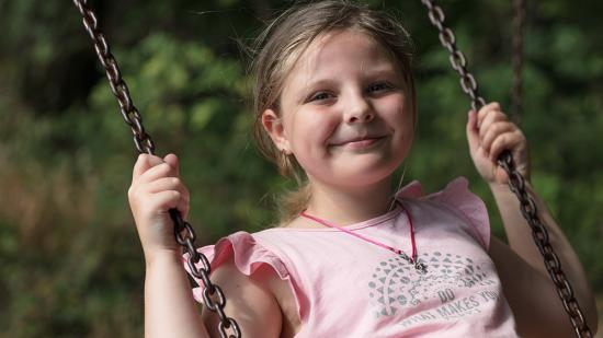 Mädchen lacht in die Kamera, während sie auf einer Schaukel sitzt und schaukelt