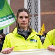 Hannah Keller, Klima-Sprecherin bei GLOBAL 2000, bei einer Demo, sie hät ein Banner in den Händen, dahinter sind Fahnen, daneben angedeutet weitere Menschen