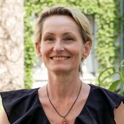 Patricia Lorenz trägt kurze blonde Haare und eine schwarze Bluse. Sie lächelt in die Kamera