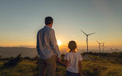 Vater und Kind blicken Richtung Sonnenaufgang in Landschaft mit Windrädern