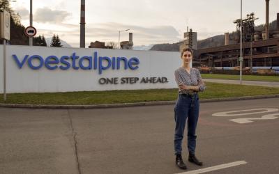 Anna Leitner steht auf der Straße vor dem Schild der Voestalpine