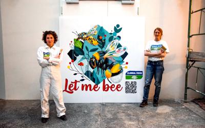 zwei Aktivistinnen mit Pinsel in den Händen stehen vor dem Bild, dass sie gerade gemalt haben. Darauf zu sehen sind zwei Bienen und der Schriftzug "Let me bee"