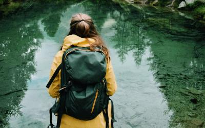 Frau mit Rucksack schaut auf einen See und Berge, von hinten