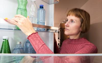 Frau öffnet Kühlschrank, in dem Mineralwasserflaschen stehen