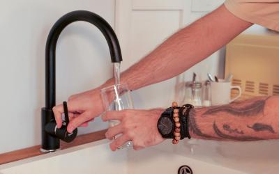 Eine Person lässt Wasser in ihr Wasserglas über den Wasserhahn fließen
