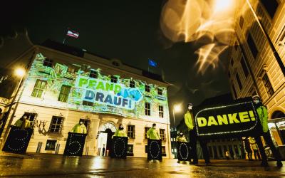 Beamer-Aktion mit dem Pfand-drauf-Logo. Davor stehen Aktivist*innen mit einem Banner, auf dem "Danke" steht.