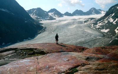 Mann steht alleine auf einem Berg, im Hindergrund ein Gletscher
