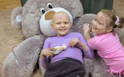 Zwei Kinder liegen auf einem großen Stoffbären und lachen in die Kamera