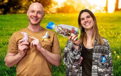 Ein junger Mann und eine junge Frau halten Schoko-Osterhasen in die Kamera und lachen