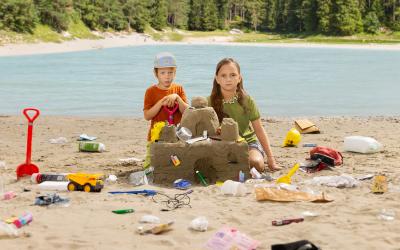 2 Kinder bauen Sandburg mit Müll drin, schauen traurig