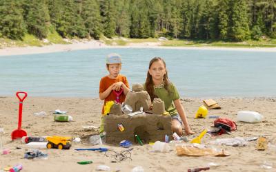 2 Kinder bauen eine Sandburg mit Müll vor österreichischer Landschaft