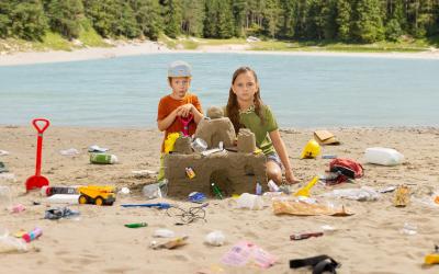 2 Kinder bauen eine Sandburg mit Müll vor österreichischer Landschaft