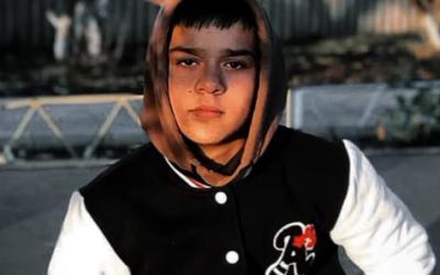 Junge mit schwarzen Haaren und Schwartz weißer Jacke sitzt auf einer Bank 