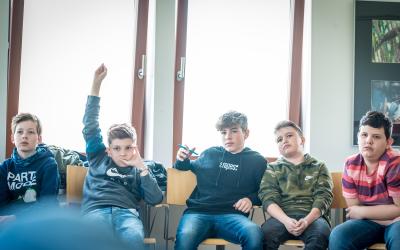 Schüler sitzen in einer Reihe, einer hebt die Hand