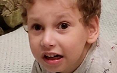 Kleiner Junge mit lockigen Haaren liegt auf dem Bett