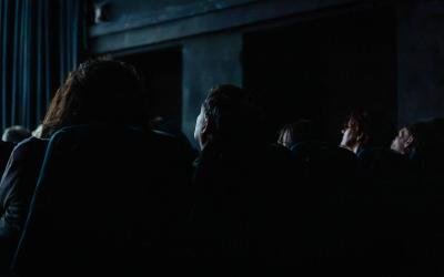 In einem sehr dunklen Kinosaal sieht man schemenhaft Menschen sitzen