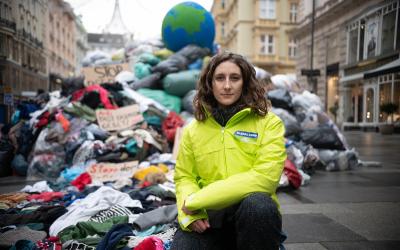 Anna Leitner, Ressourcensprecherin von GLOBAL 2000, hockt vor Müllberg mit Kleidung in der Wiener Innenstadt
