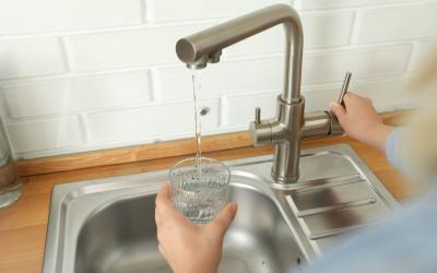 Wasserhahn über Spüle, aus dem Wasser in ein Glas fließt, Hand hält das Glas und betätigt den Hebel
