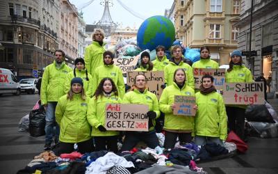 Aktivist:innen von GLOBAL 2000 protestieren mit Kleidungsberg und Erdball für Anti-Fast-Fashion-Gesetz