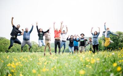 Gruppe von Menschen springt auf einer Wiese mit gelben Blumen in die Luft und hebt die Arme