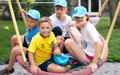 Vier Kinder mit bemalten Gesichtern sitzen gemeinsam auf einer großen runden Nestschaukel im Freien