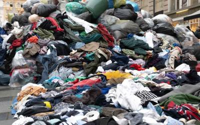 Großer Haufen ausgebrauchter Kleidung auf einer Straße mit einem großen Globus als Symbol im Hintergrund bei einer Aktion von GLOBAL 2000