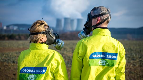 Stopp AKW Mochovce - Zwei Personen stehen vor einem AKW und sehen sich an, sie tragen GLOBAL 2000 Jacken und Schutzmasken