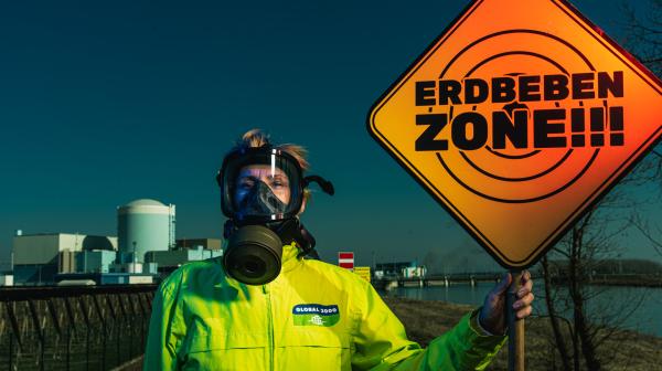 Aktivistin steht in Global 2000-Jacke vor Krsko-Reaktor mit Schild "Erdbebengebiet"