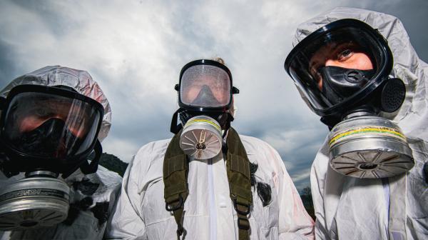 Drei Aktivist:innen mit Gasmaske und Strahlenschutzanzügen schauen in die Kamera