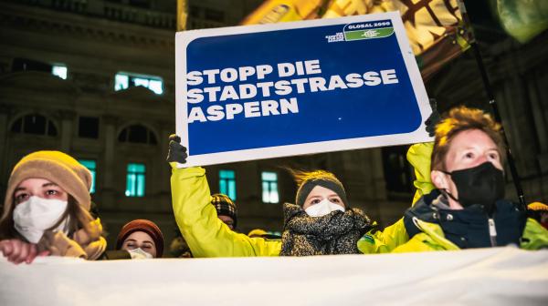 Demonstrantin bei Demo hält Schild mit "Stoppt die Stadtstrasse Aspern"
