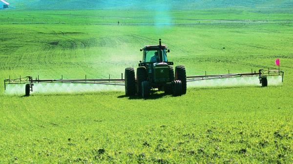 Ein Traktor versprüht Pestozide auf einem grünen Feld