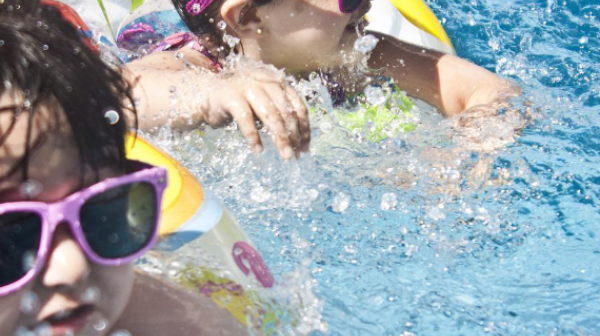 zwei Kinder schwimmen mit Schwimmreifen und Sonnenbrillen