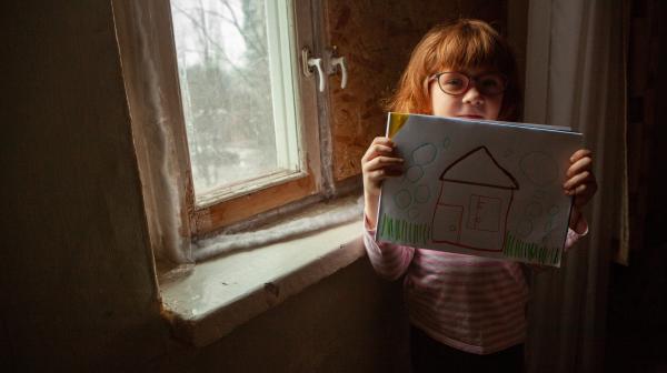 Ukrainisches Mädchen hält Zeichnung mit Haus in die Kamera