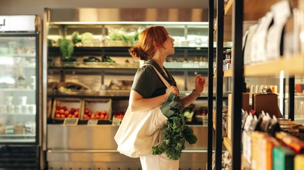 Frau steht vor Supermarktregal und sucht nach dem richtigen Produkt
