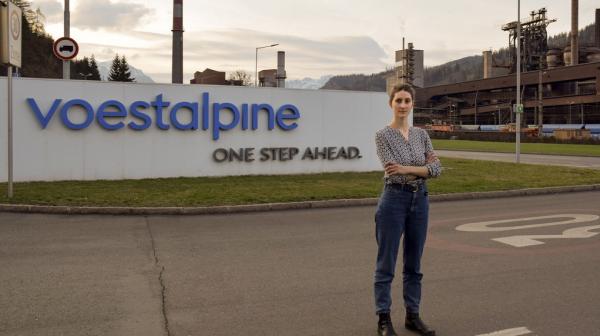 Anna Leitner steht auf der Straße vor dem Schild der Voestalpine