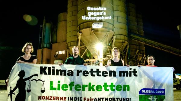Aktivist:innen stehen vor der Firma Holcim und halten ein großes Banner in die Kamera. Darauf steht "Klima retten mit Lieferketten"