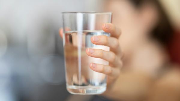 Person (unscharf im Hintergrund) hält Wasserglas