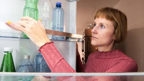 Frau öffnet Kühlschrank, in dem Mineralwasserflaschen stehen