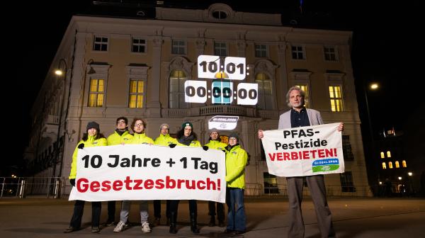 Aktivist:innen stehen vor dem Bundesministerium und halten einen Banner in der Hand: "10 Jahre + 1 Tag Gesetzesbruch"