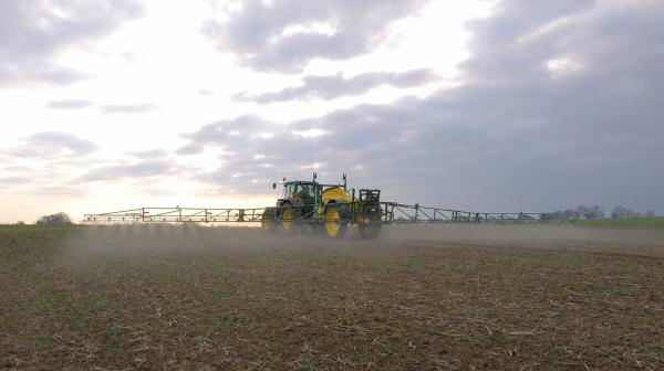Traktor spritzt Pestizide auf einem Feld. 