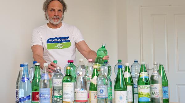 Helmut Burtscher-Schaden in einem GLOBAL 2000-T-Shirt mit allen getesteten Mineralwasserflaschen