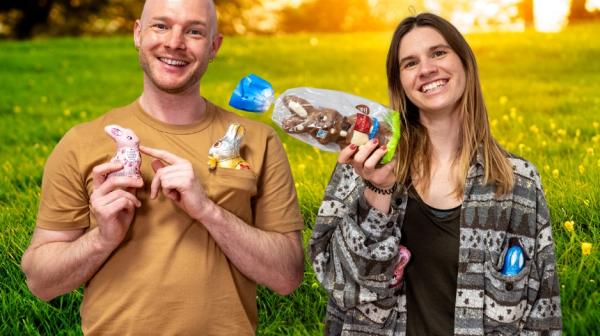 Ein junger Mann und eine junge Frau halten Schoko-Osterhasen in die Kamera und lachen